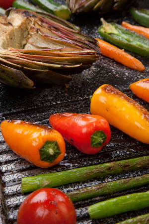 Assorted grilled vegetables - zucchini, asparagus, artichokes, mini pepper, jalapeno, tomatoes, and carrots - on griddle.の写真素材