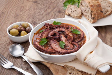 Bowl of delicious octopus and red wine stew - traditional Mediterranean dish. Fresh bread, olives, and red wine.の写真素材