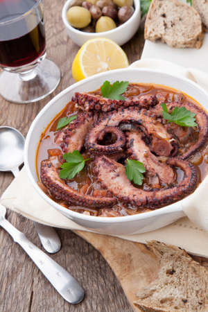 Bowl of delicious octopus and red wine stew - traditional Mediterranean dish. Fresh bread, olives, and red wine.の写真素材