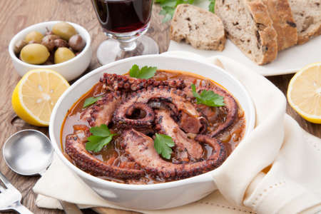 Bowl of delicious octopus and red wine stew - traditional Mediterranean dish. Fresh bread, olives, and red wine.の写真素材