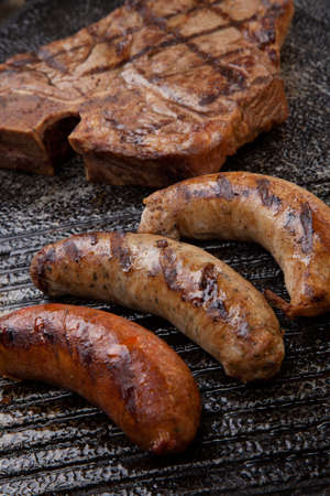 Summer grill - grilled sausages and T-bone steak - on griddle.の写真素材