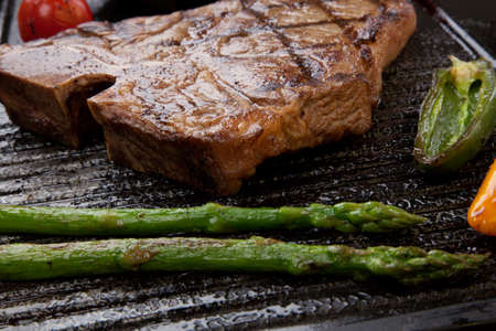 Summer grill - grilled T-bone steak and assorted grilled vegetables - asparagus, mini pepper, and tomatoes - on griddle.の写真素材