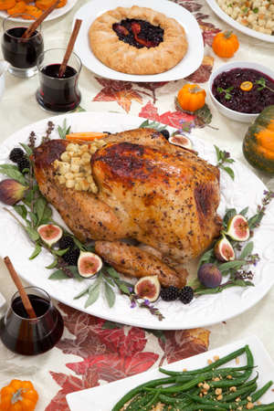 Dinner table with roasted Thanksgiving turkey is ready to feast. Turkey is garnished with fresh figs, blackberries, sage, and basil. Sided dishes, pumpkinks, flowers, and red wine cocktails.の写真素材