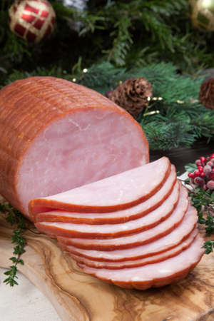 Roasted ham with fresh thyme for Christmas party. XMas tree in the background, surrounded by ornaments. Rustic style.の写真素材