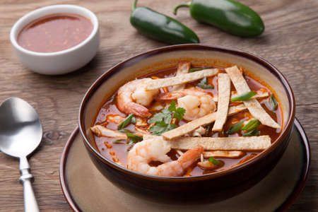 Bowl of hot delicious shrimp tortilla soup garnished with green onion, fresh cilantro, and salsa.の写真素材