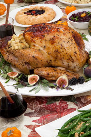 Dinner table with roasted Thanksgiving turkey is ready to feast. Turkey is garnished with fresh figs, blackberries, sage, and basil. Sided dishes, pumpkinks, flowers, and red wine cocktails.の写真素材