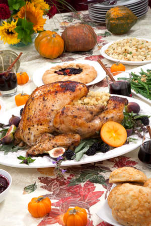 Dinner table with roasted Thanksgiving turkey is ready to feast. Turkey is garnished with fresh figs, blackberries, sage, and basil. Sided dishes, pumpkinks, flowers, and red wine cocktails.の写真素材