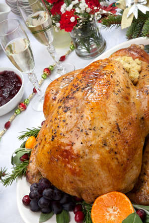 Roasted herb rubbed turkey garnished with fresh grapes, oranges, and cranberry is ready for Christmas dinner. Ornaments, Champagne, candles, and other Christmas decorations on feast table.の写真素材
