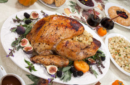 Dinner table with roasted Thanksgiving turkey is ready to feast. Turkey is garnished with fresh figs, blackberries, sage, and basil. Sided dishes, pumpkinks, flowers, and red wine cocktails.の写真素材