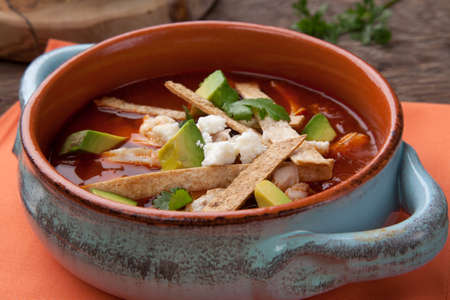Bowl of hot delicious spicy chicken tortilla soup garnished with crumbled queso fresco cheese, diced avocado, and fresh cilantro.の写真素材