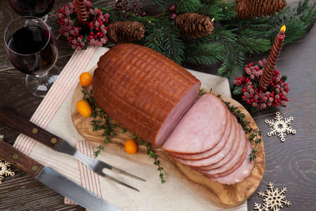 Roasted ham with fresh thyme for Christmas party. XMas tree in the background, surrounded by ornaments. Rustic style.の写真素材