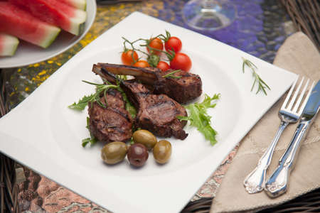 Grilled lamb chops served with cherry tomatoes and olives. Watermelon and wine. Outside dinner in a garden.の写真素材