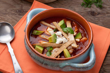 Bowl of hot delicious spicy chicken tortilla soup garnished with crumbled queso fresco cheese, diced avocado, and fresh cilantro.の写真素材
