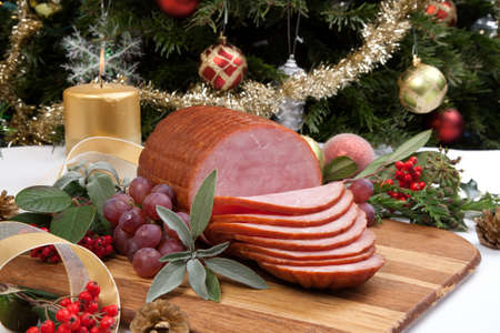Roasted ham with fresh thyme for Christmas party. XMas tree in the background, surrounded by ornaments. Rustic style.の写真素材