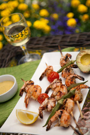 Plate of grilled shrimps skewers with grilled vegetables and avocado. Served with lemon and lemon butter sauce. Outside dinner in a garden.の写真素材
