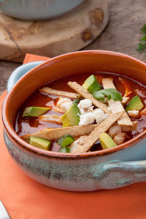 Bowl of hot delicious spicy chicken tortilla soup garnished with crumbled queso fresco cheese, diced avocado, and fresh cilantro.の写真素材