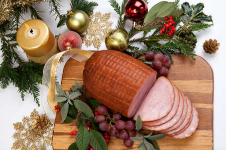Roasted ham with fresh thyme for Christmas party. XMas tree in the background, surrounded by ornaments. Rustic style.の写真素材