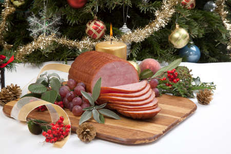 Roasted ham with fresh thyme for Christmas party. XMas tree in the background, surrounded by ornaments. Rustic style.の写真素材