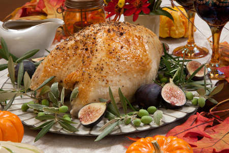 Whole roasted turkey breast, Mediterranean style, garnished with fresh figs, olives, and herbs. Surrounded by pumpkins, candles, red wine, and ornaments. Thanksgiving theme.の写真素材