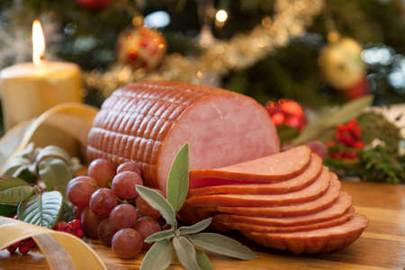 Roasted ham with fresh thyme for Christmas party. XMas tree in the background, surrounded by ornaments. Rustic style.の写真素材