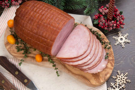 Roasted ham with fresh thyme for Christmas party. XMas tree in the background, surrounded by ornaments. Rustic style.の写真素材