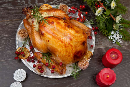 Rustic style roasted Christmas turkey garnished with roasted garlic, lemon, and rosehips. Surrounded with rustic Christmas ornaments, candles, wine, flowers, and Christmas tree in the background.の写真素材
