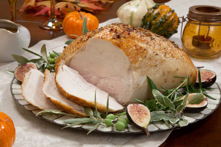 Carving whole roasted turkey breast, Mediterranean style, garnished with fresh figs, olives, and herbs. Surrounded by pumpkins, candles, red wine, and ornaments. Thanksgiving theme.の写真素材