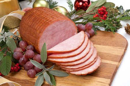 Roasted ham with fresh thyme for Christmas party. XMas tree in the background, surrounded by ornaments. Rustic style.の写真素材