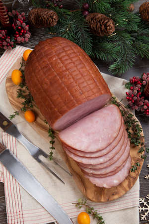 Roasted ham with fresh thyme for Christmas party. XMas tree in the background, surrounded by ornaments. Rustic style.の写真素材