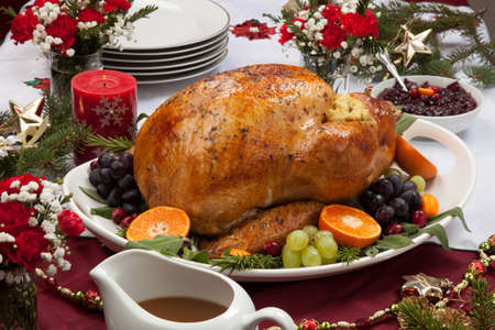Roasted herb rubbed turkey garnished with fresh grapes, oranges, and cranberry is ready for Christmas dinner. Ornaments, Champagne, candles, and other Christmas decorations on feast table.の写真素材
