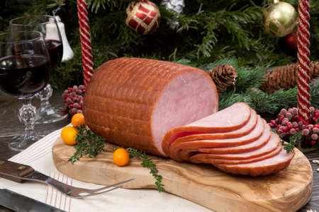 Roasted ham with fresh thyme for Christmas party. XMas tree in the background, surrounded by ornaments. Rustic style.の写真素材