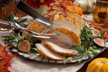 Carving whole roasted turkey breast, Mediterranean style, garnished with fresh figs, olives, and herbs. Surrounded by pumpkins, candles, red wine, and ornaments. Thanksgiving theme.の写真素材