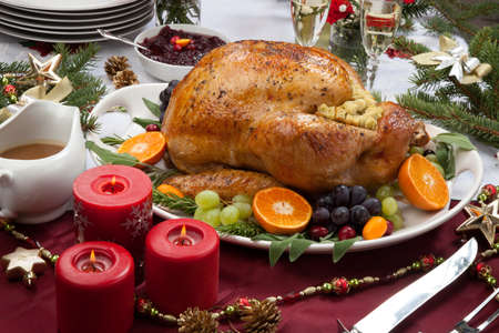 Roasted herb rubbed turkey garnished with fresh grapes, oranges, and cranberry is ready for Christmas dinner. Ornaments, Champagne, candles, and other Christmas decorations on feast table.の写真素材