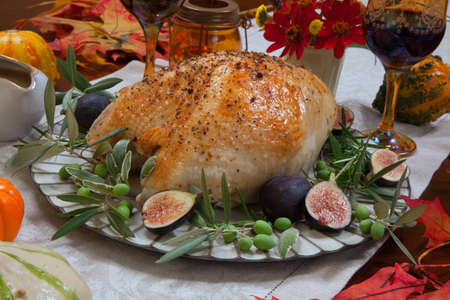 Whole roasted turkey breast, Mediterranean style, garnished with fresh figs, olives, and herbs. Surrounded by pumpkins, candles, red wine, and ornaments. Thanksgiving theme.の写真素材