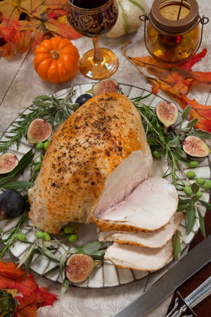 Carving whole roasted turkey breast, Mediterranean style, garnished with fresh figs, olives, and herbs. Surrounded by pumpkins, candles, red wine, and ornaments. Thanksgiving theme.の写真素材