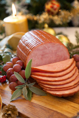 Roasted ham with fresh thyme for Christmas party. XMas tree in the background, surrounded by ornaments. Rustic style.の写真素材