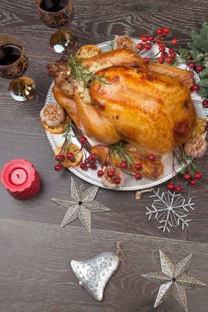 Rustic style roasted Christmas turkey garnished with roasted garlic, lemon, and rosehips. Surrounded with rustic Christmas ornaments, candles, wine, flowers, and Christmas tree in the background.の写真素材