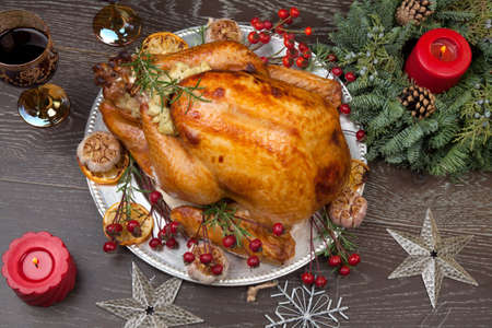 Rustic style roasted Christmas turkey garnished with roasted garlic, lemon, and rosehips. Surrounded with rustic Christmas ornaments, candles, wine, flowers, and Christmas tree in the background.の写真素材
