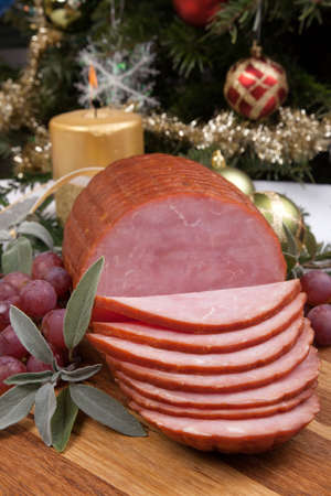Roasted ham with fresh thyme for Christmas party. XMas tree in the background, surrounded by ornaments. Rustic style.の写真素材