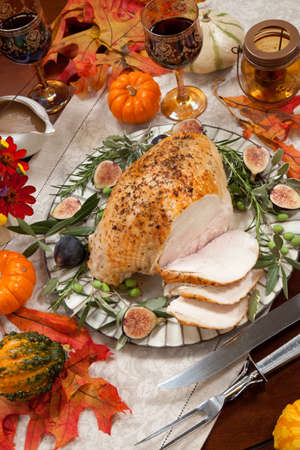 Carving whole roasted turkey breast, Mediterranean style, garnished with fresh figs, olives, and herbs. Surrounded by pumpkins, candles, red wine, and ornaments. Thanksgiving theme.の写真素材