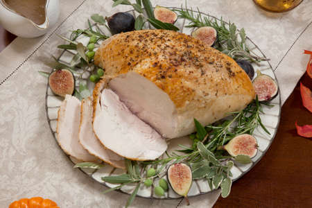 Carving whole roasted turkey breast, Mediterranean style, garnished with fresh figs, olives, and herbs. Surrounded by pumpkins, candles, red wine, and ornaments. Thanksgiving theme.の写真素材
