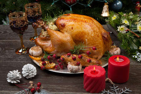 Rustic style roasted Christmas turkey garnished with roasted garlic, lemon, and rosehips. Surrounded with rustic Christmas ornaments, candles, wine, flowers, and Christmas tree in the background.の写真素材