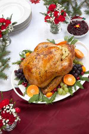 Roasted herb rubbed turkey garnished with fresh grapes, oranges, and cranberry is ready for Christmas dinner. Ornaments, Champagne, candles, and other Christmas decorations on feast table.の写真素材