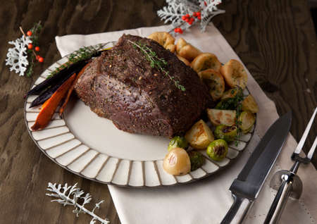 Uncut piece pf peppercorn roast beef with herbed Yorkshire puddings garnished with roasted vegetables.の写真素材