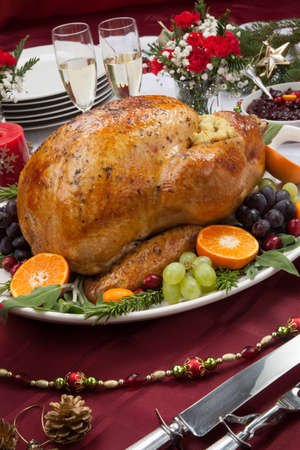 Roasted herb rubbed turkey garnished with fresh grapes, oranges, and cranberry is ready for Christmas dinner. Ornaments, Champagne, candles, and other Christmas decorations on feast table.の写真素材