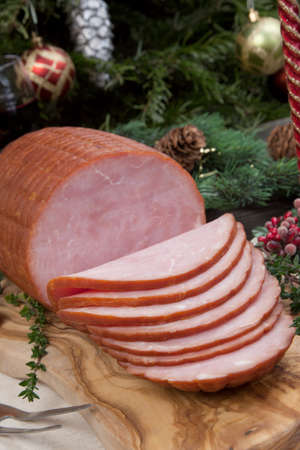 Roasted ham with fresh thyme for Christmas party. XMas tree in the background, surrounded by ornaments. Rustic style.の写真素材