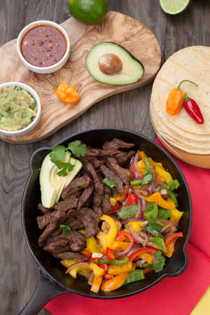 Beef fajitas with bell pepper, onion, and avocado in cast iron skillet ready to be served.の写真素材