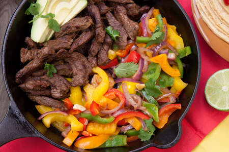 Beef fajitas with bell pepper, onion, and avocado in cast iron skillet ready to be served.の写真素材