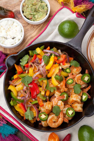 Shrimp fajitas with bell pepper, onion, and jalapeno in cast iron skillet ready to be served. Guacamole, salse, and tortillas.の写真素材