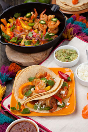 Two shrimp fajitas with bell pepper, onion, and jalapeno in a plate and shrimp fajitas in a cast iron skillet ready to be served. Guacamole, salsa, and tortillas.の写真素材